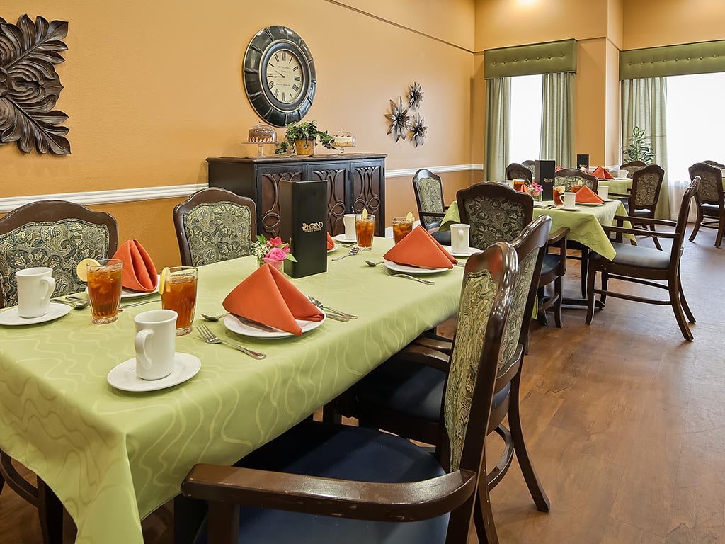 A well-set dining room with tables prepared for guests, featuring green tablecloths and red napkins.