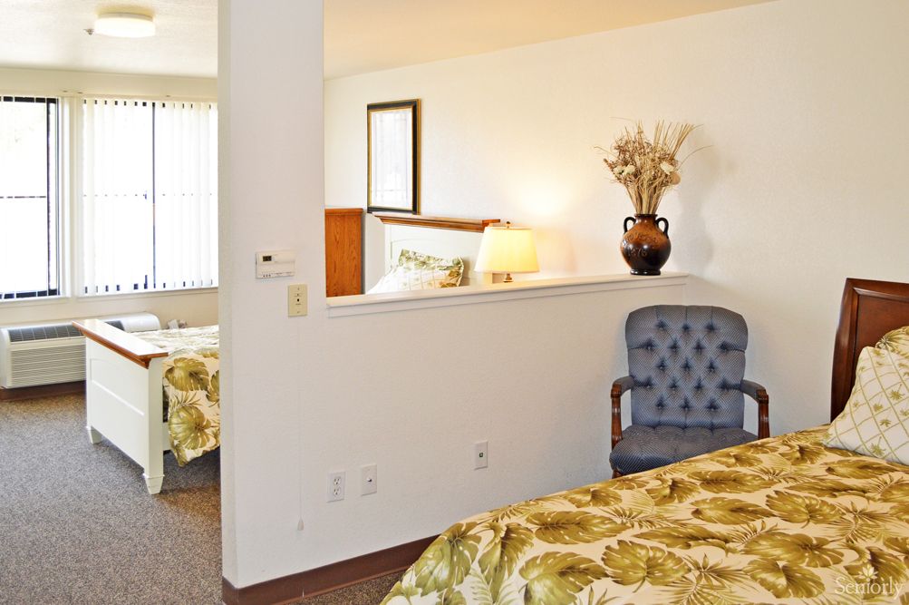 A well-lit hotel room featuring a cozy bed, a decorative vase on a shelf, and an upholstered chair.