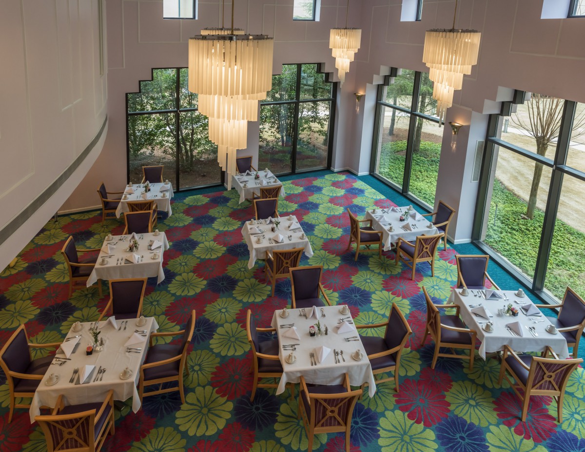 A well-lit restaurant interior with elegantly set tables and colorful carpet.