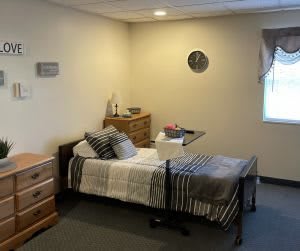 A cozy bedroom with a bed, dressers, and a wall clock.