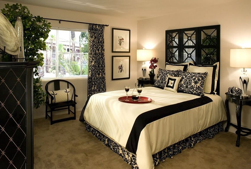 A stylish and cozy bedroom with elegant decor, featuring a neatly made bed with patterned bedding, a bedside lamp, and an armchair by the window.