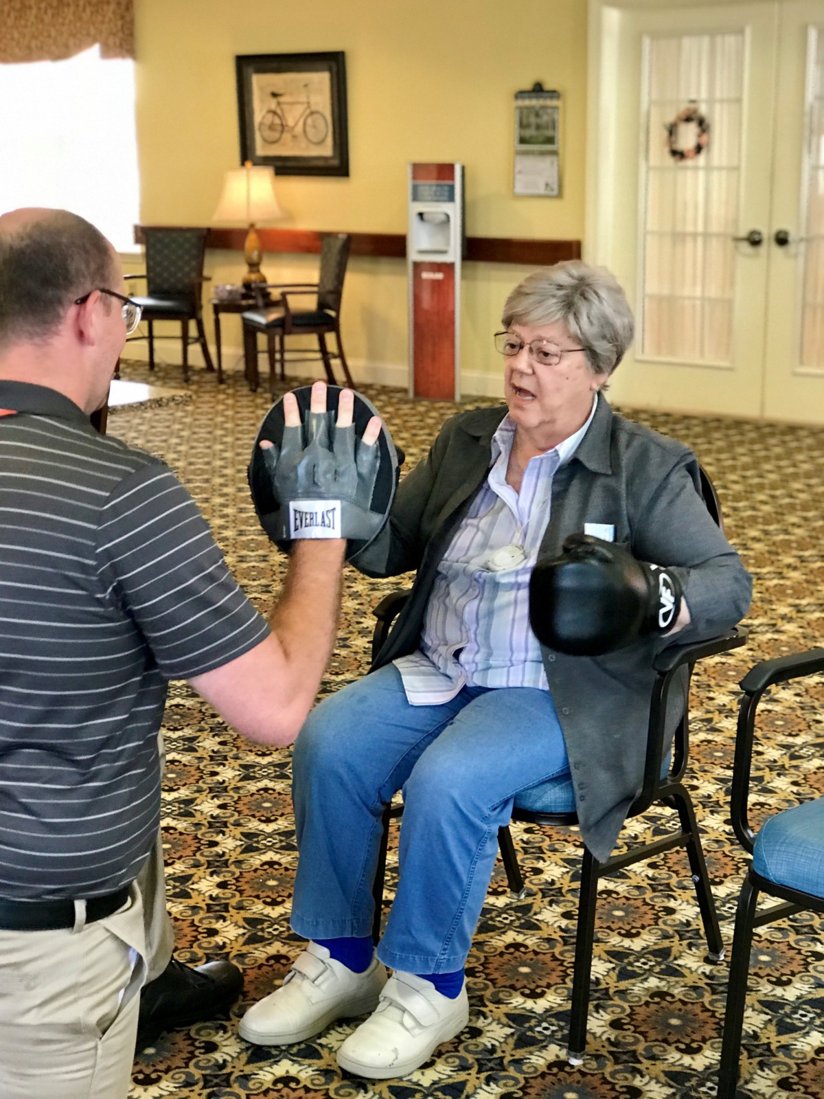 An elderly woman participates in a boxing exercise session with a trainer.