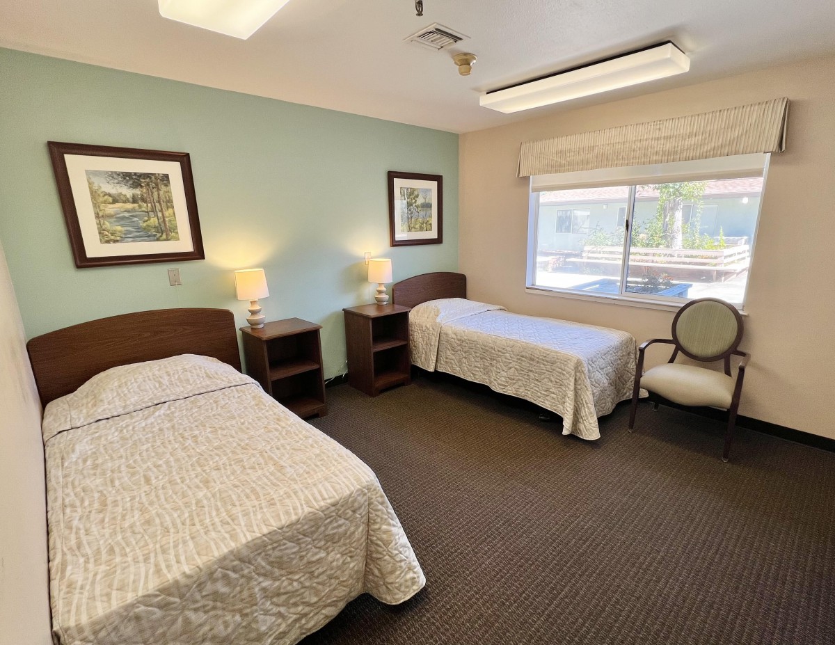 A neat and clean bedroom with two single beds, decorated with artwork and illuminated by natural light from a large window.