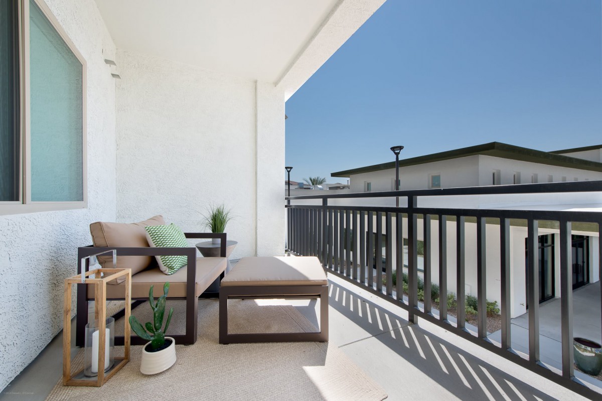 A modern balcony with comfortable seating and plants, offering a sunny urban view.
