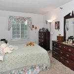 A cozy bedroom featuring a bed with a quilt, a dresser with a mirror, and various decorative elements.