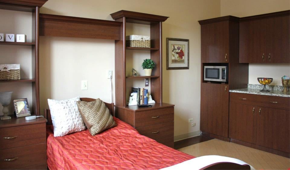A cozy bedroom with a bed, bookshelf, and microwave.
