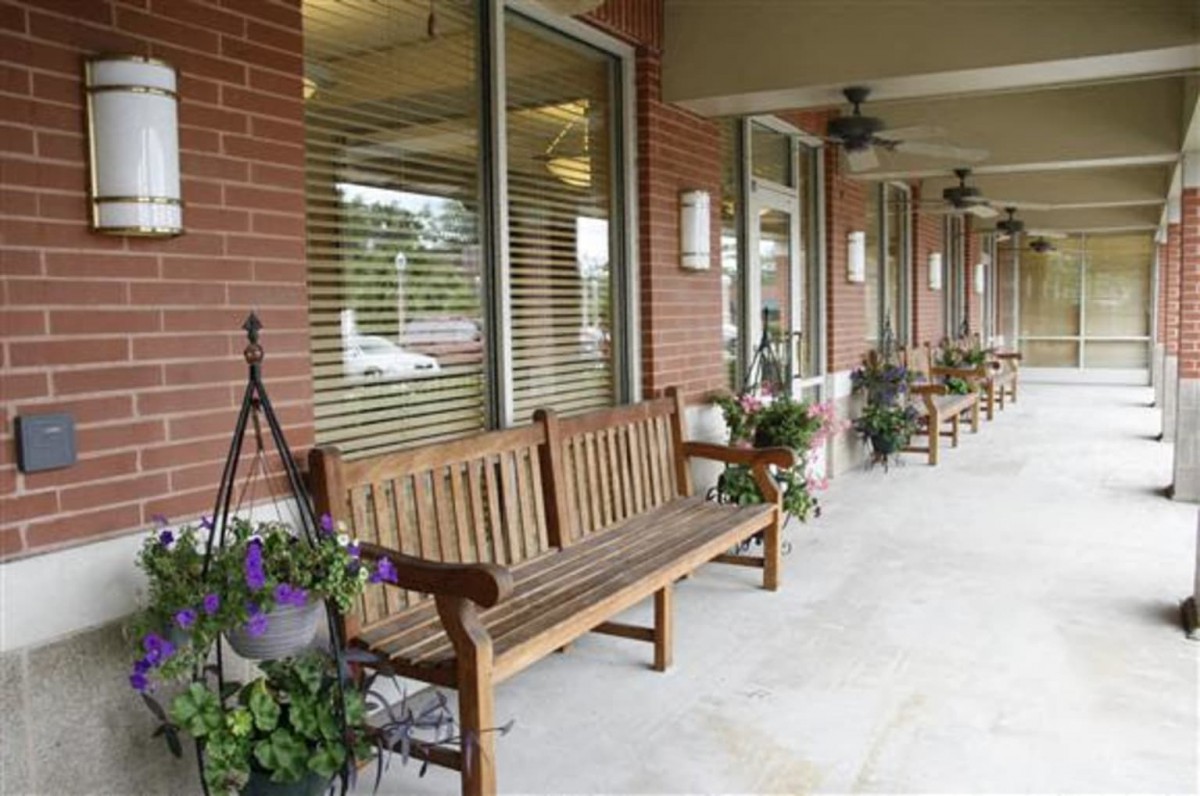 A row of wooden benches outside a brick storefront with windows and potted plants.