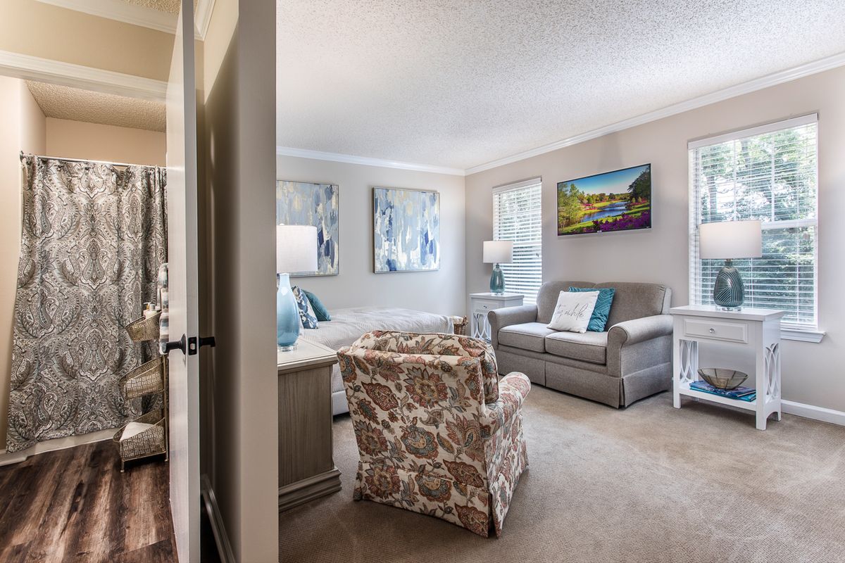 A cozy living room with modern decor, featuring a sofa and armchair, adorned with artwork and ample natural light.