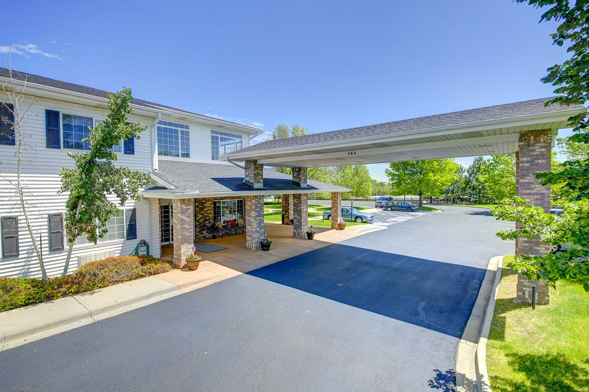 A modern building entrance with a covered driveway and surrounding greenery.
