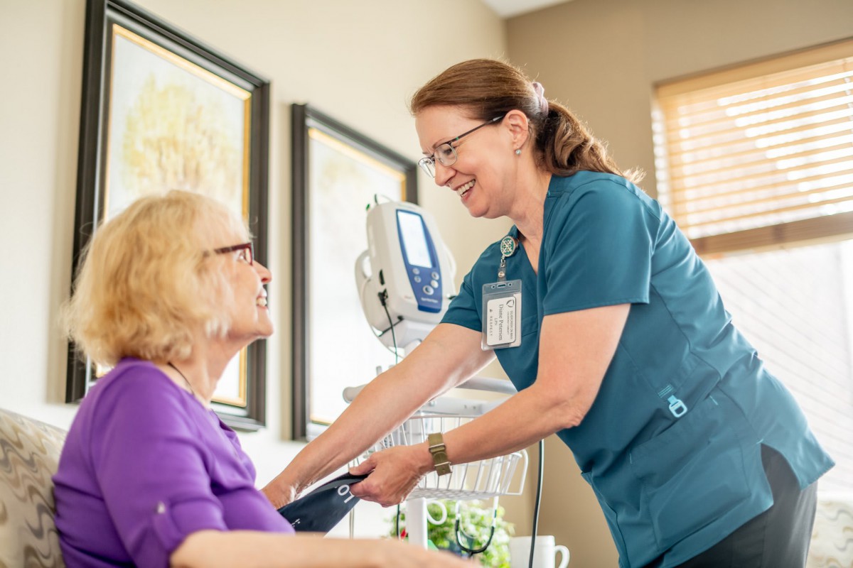 A nurse smiles while checking the blood pressure of an elderly patient in a healthcare setting.