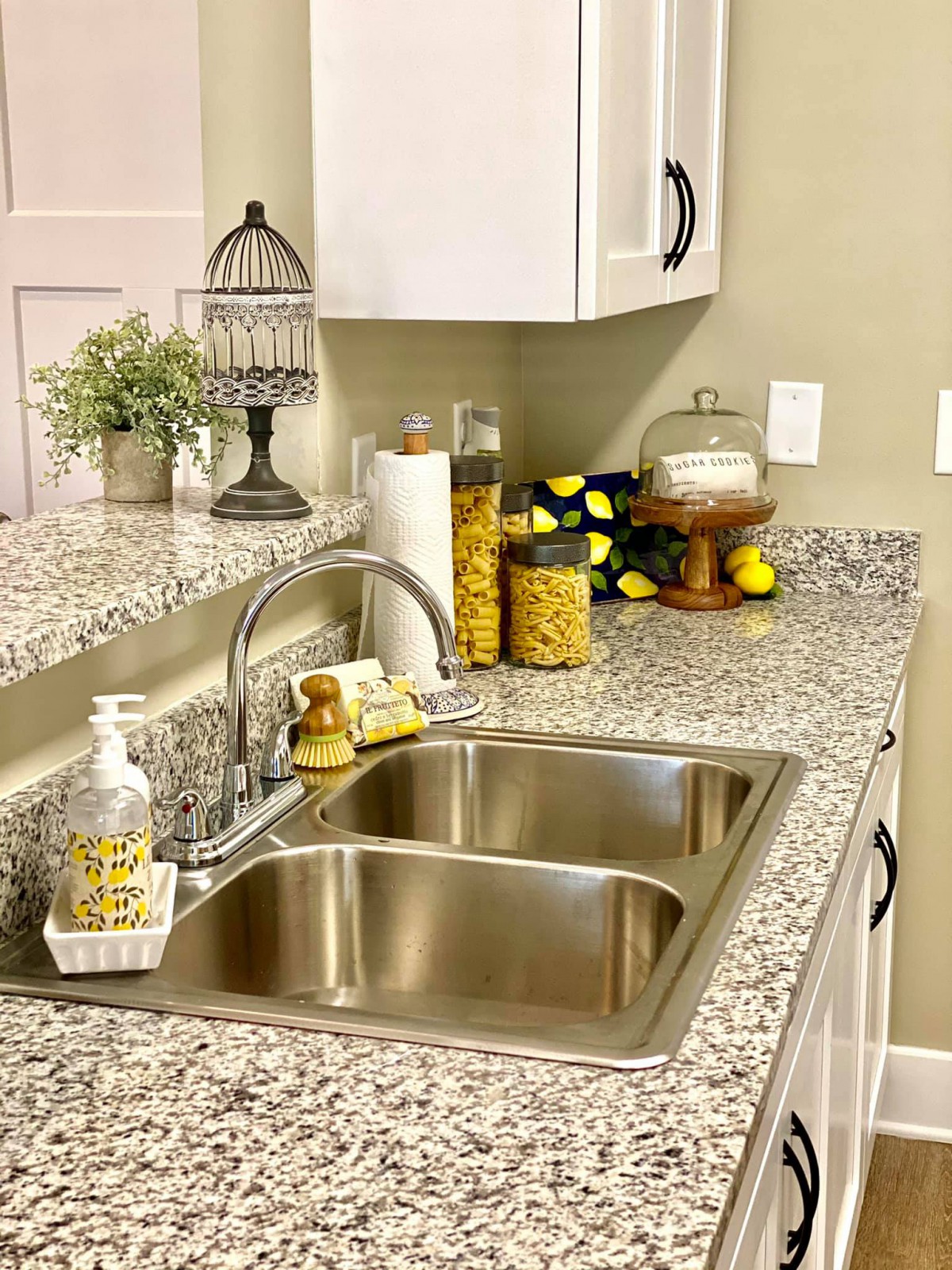A well-organized kitchen countertop featuring a double sink, decorative elements, and neatly arranged jars.