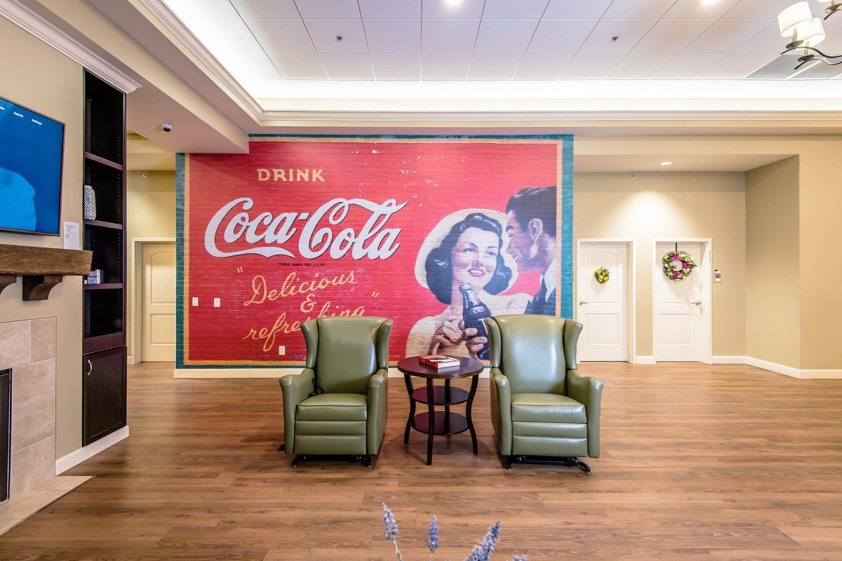 A cozy indoor setup featuring a vintage Coca-Cola advertisement poster and green armchairs.