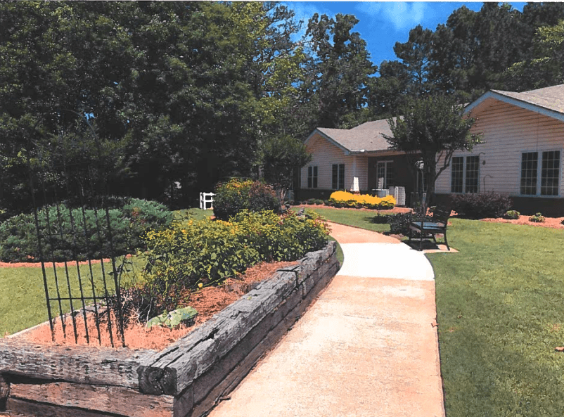A scenic garden path leading to a house surrounded by lush greenery and flowers.