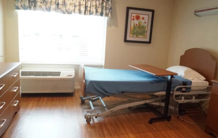 An empty hospital room featuring a single bed with blue sheets and a side table.