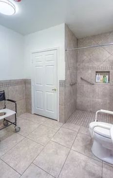 An accessible bathroom featuring a wheelchair, shower area with grab bars, and tiled walls.