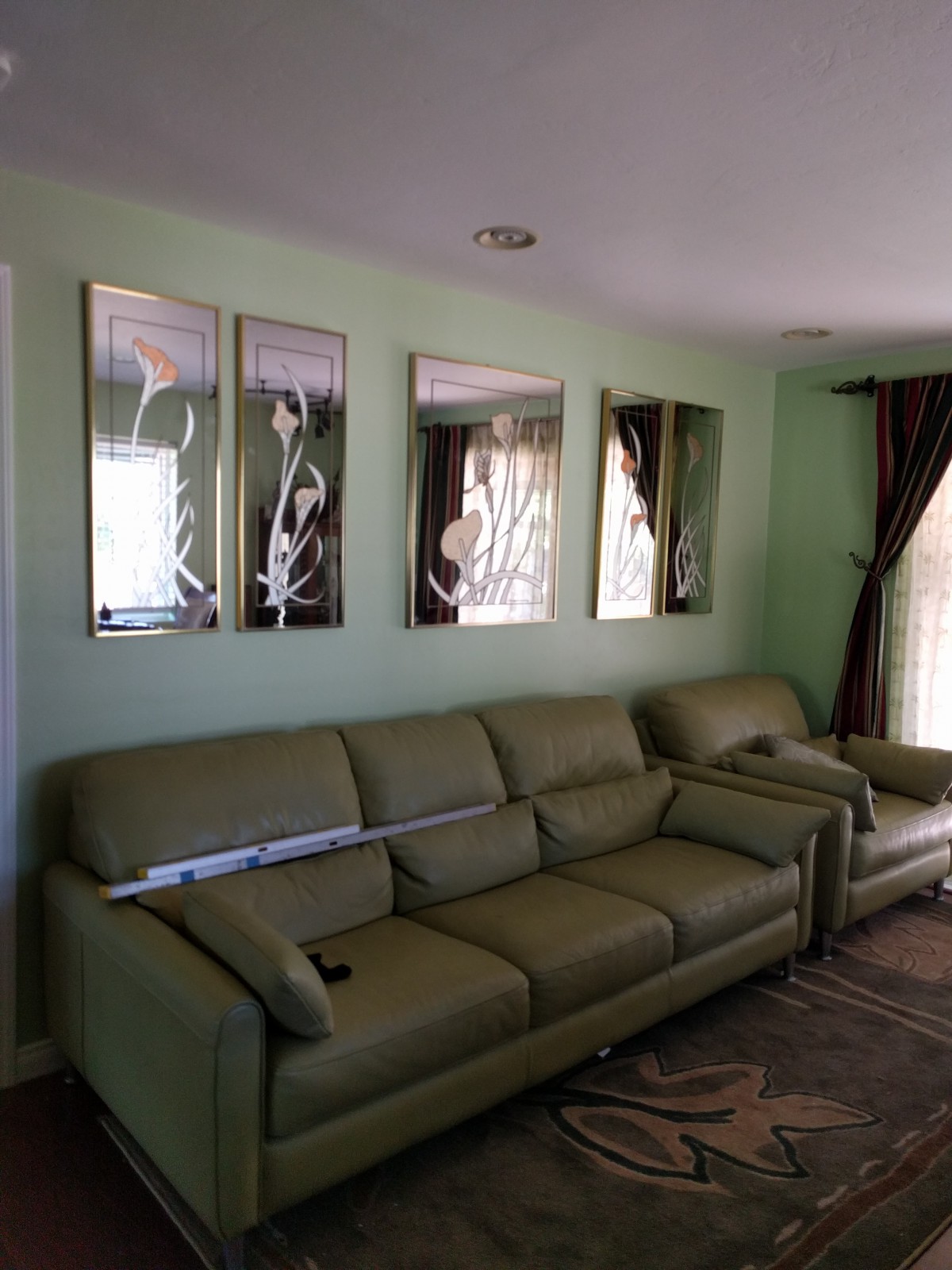 A cozy living room with green walls, featuring two green sofas and decorative mirrors on the wall.