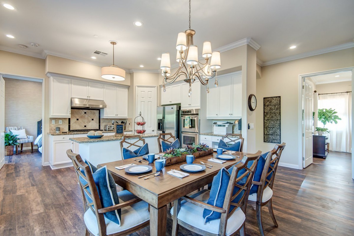 A modern kitchen and dining area with a wooden table set for a meal, complemented by a chandelier and stylish decor.