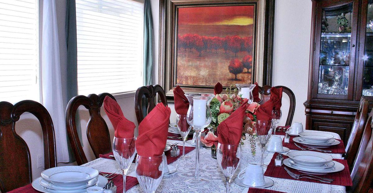 A formal dining table elegantly set with red napkins, wine glasses, and a floral centerpiece, with an abstract painting in the background.