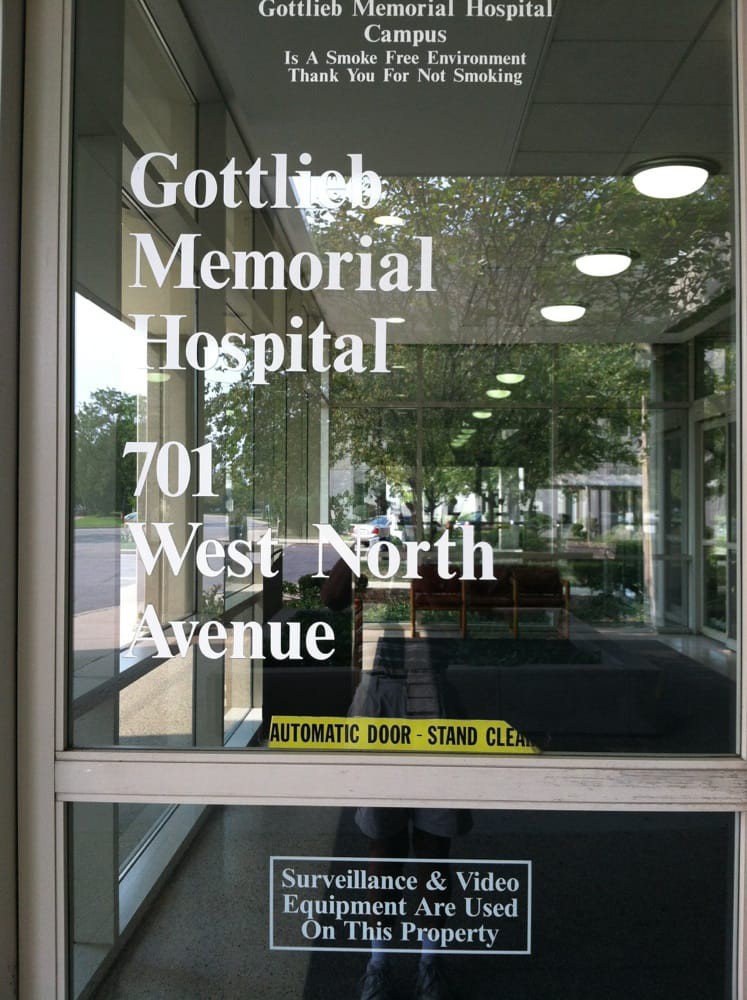 Glass entrance of Gottlieb Memorial Hospital displaying its address.