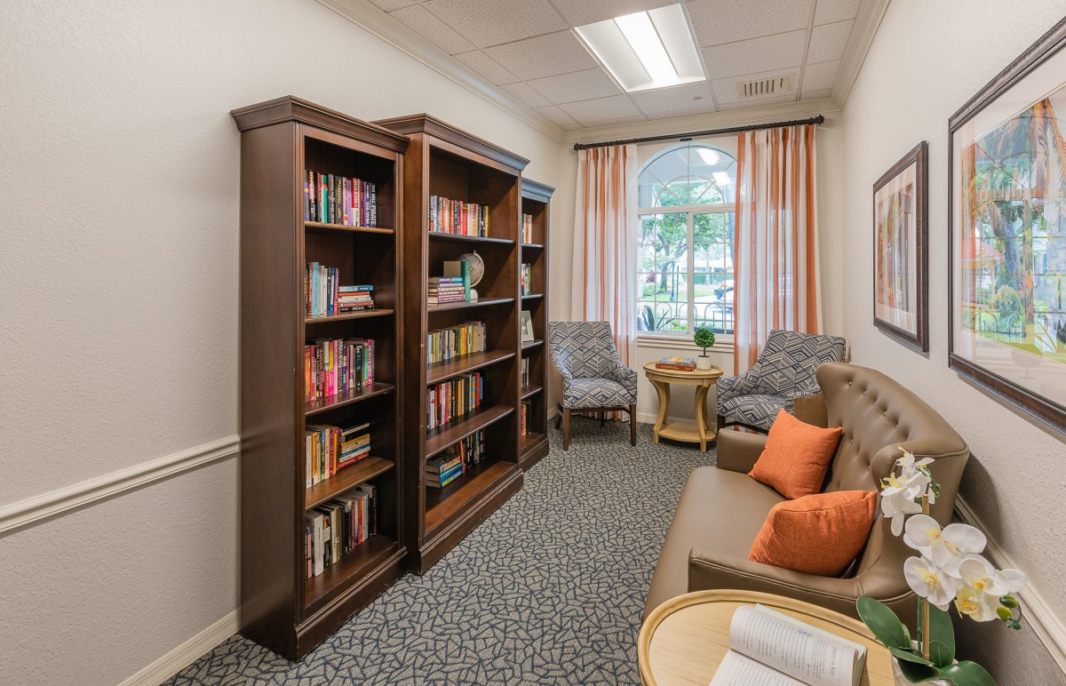 A cozy reading room featuring bookshelves filled with books, comfortable seating, and a large window with curtains.