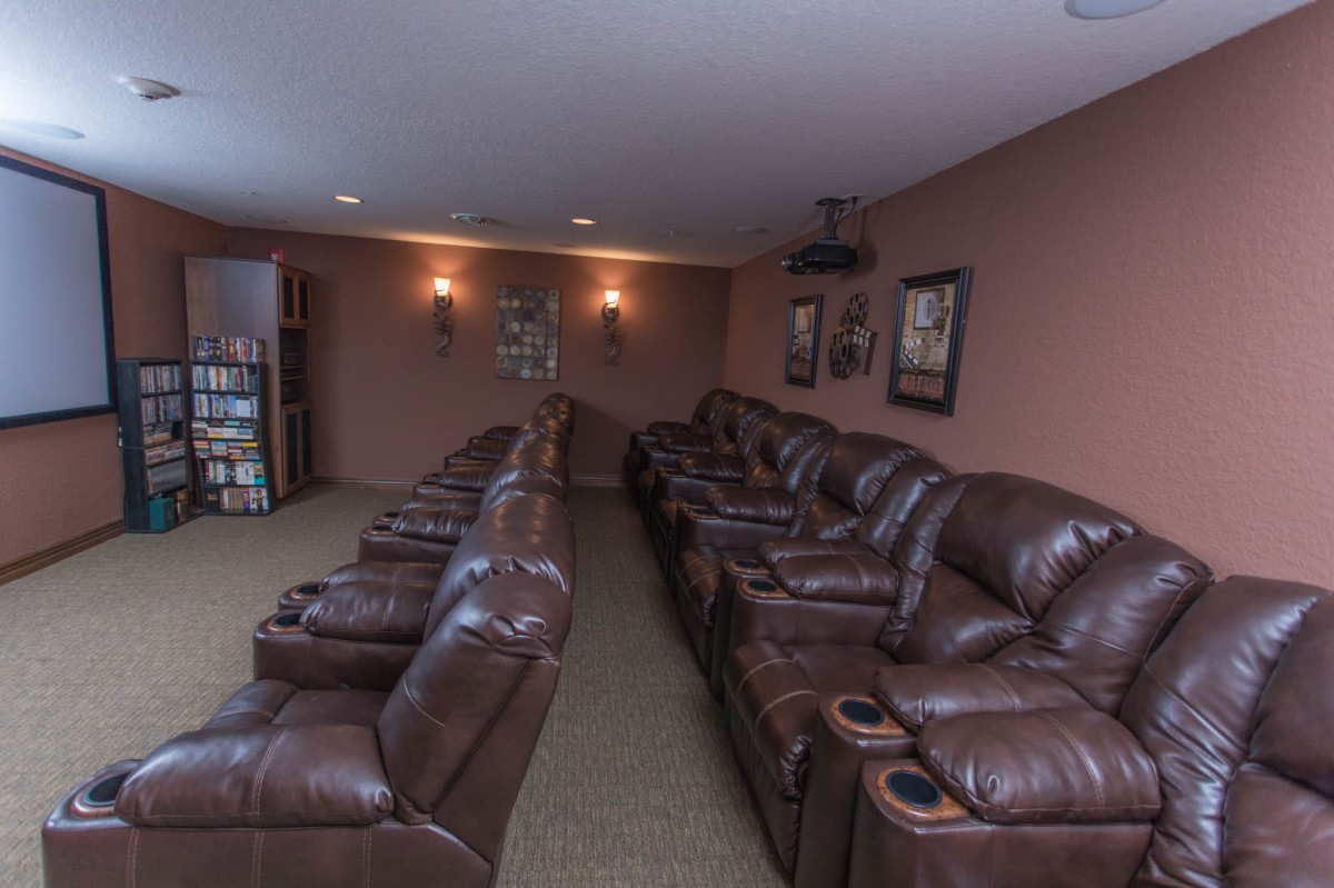 A cozy home theater with rows of leather recliners and a ceiling-mounted projector.