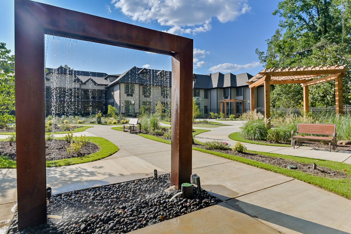 A modern residential complex with landscaped gardens and pathways under a clear blue sky.