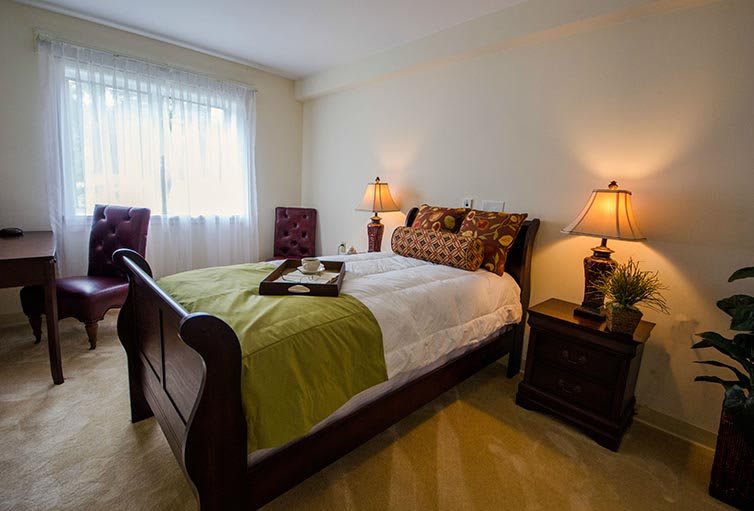A cozy bedroom with a neatly made bed, two lamps on nightstands, and natural light coming through the window.