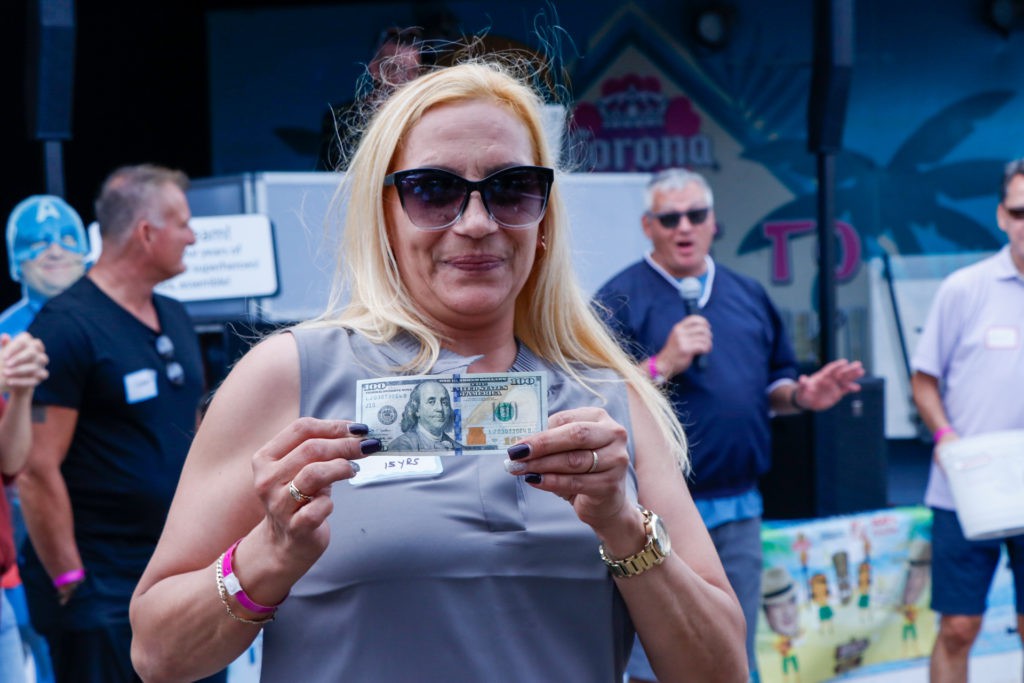 A woman wearing sunglasses holds a hundred-dollar bill at an outdoor event.