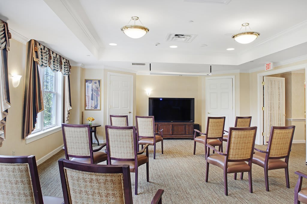 A well-lit meeting room with arranged chairs facing a large television.