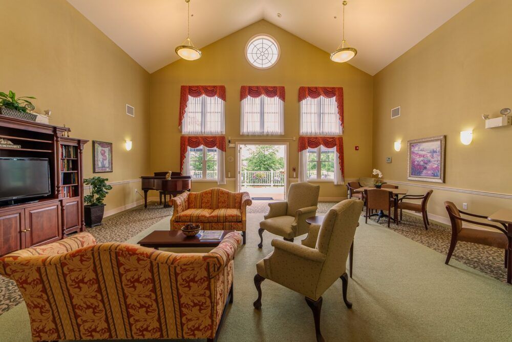 A spacious living room with high ceilings, featuring comfortable armchairs and a sofa, framed by large windows.