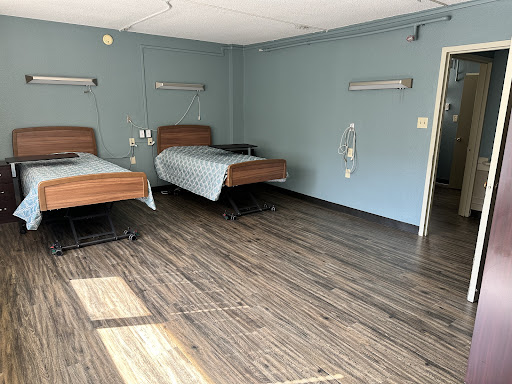 A spacious hospital room featuring two beds and a calming blue interior.
