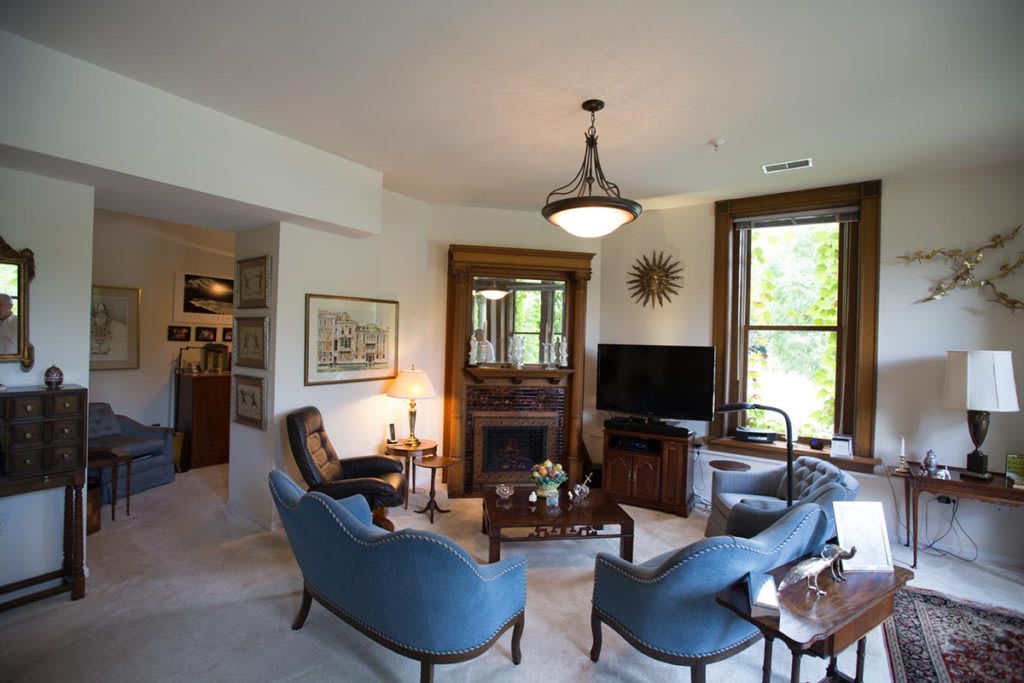 A cozy living room with blue chairs, a fireplace, and large windows offering natural light.