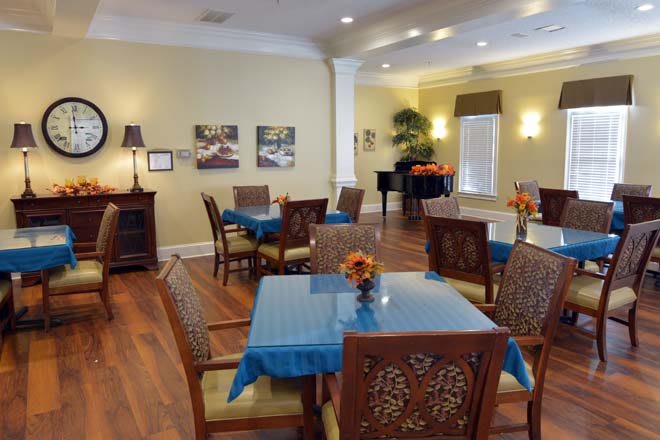 A well-lit dining room with wooden floors and neatly arranged tables and chairs.