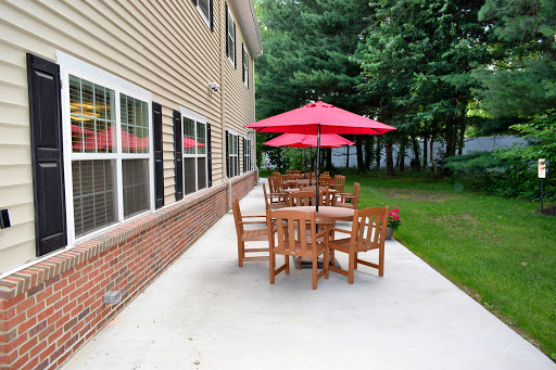 A cozy outdoor patio area featuring a wooden table and chairs, shaded by a vibrant red umbrella.