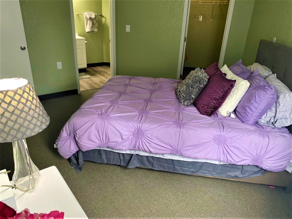 A cozy bedroom with green walls and a bed adorned with purple bedding and multiple pillows.