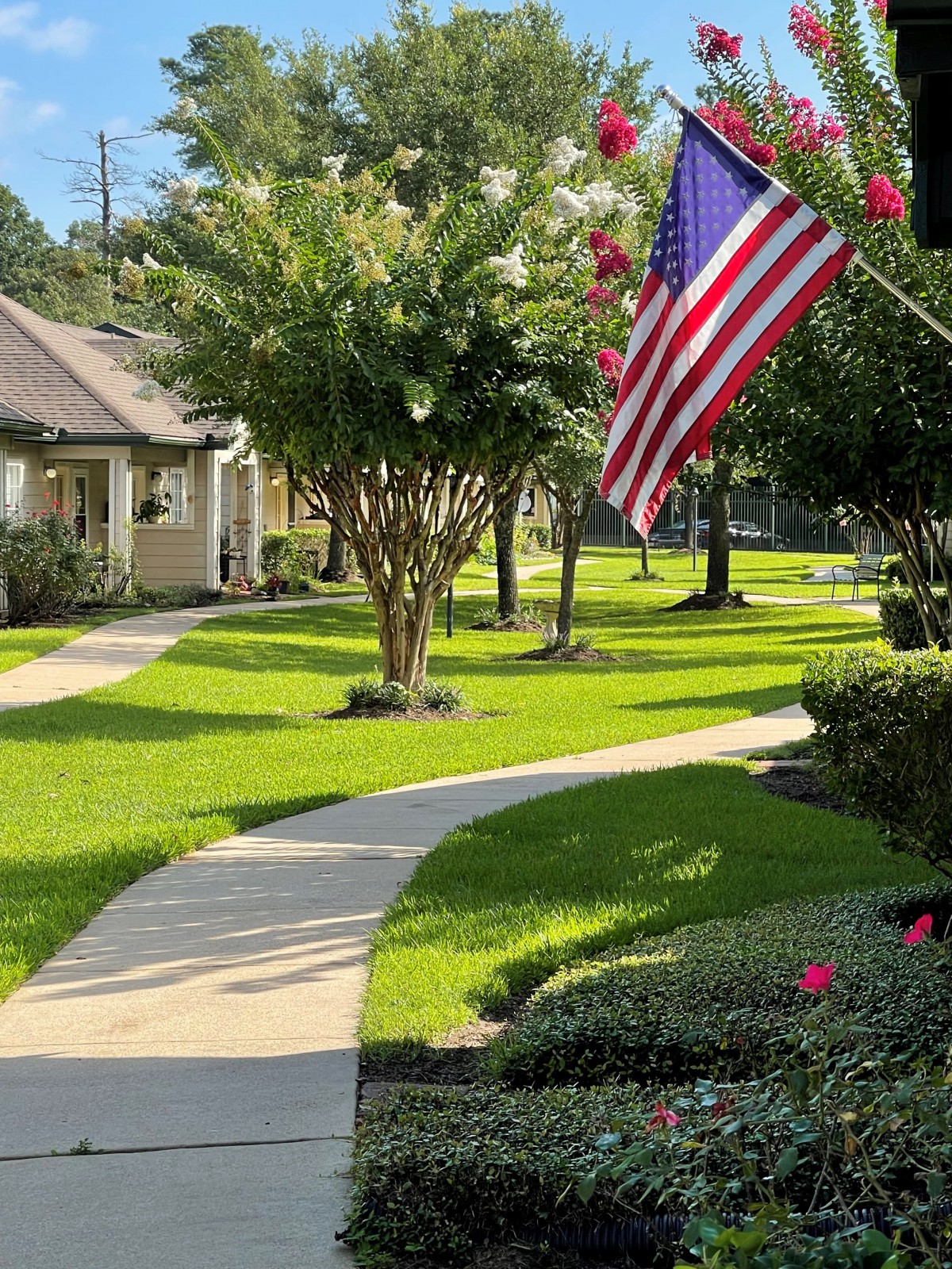A scenic pathway lined with trees and an American flag, surrounded by well-maintained greenery.