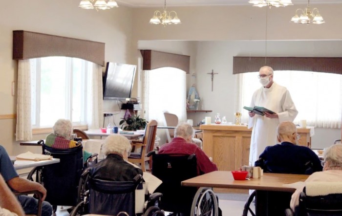 A priest conducts a religious service for elderly residents in a nursing home setting.