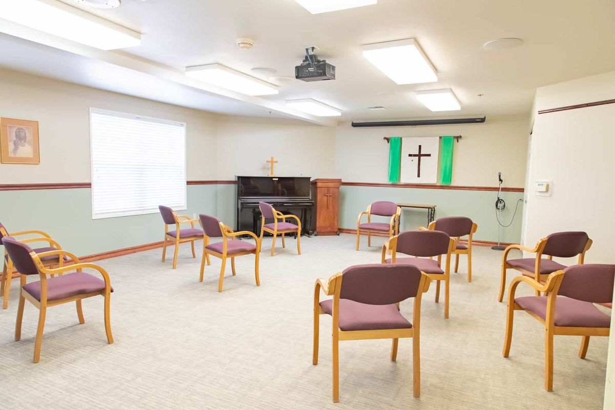An empty church meeting room with chairs arranged in a circle, featuring a cross and green banners on the wall.