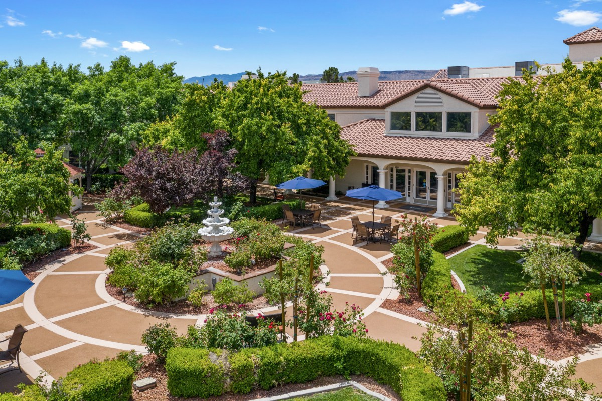 A beautifully landscaped garden with a central fountain and seating areas under umbrellas.