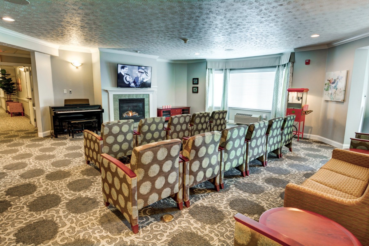 A cozy theater room with patterned armchairs, a piano, and a popcorn machine.