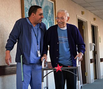 A caregiver assists an elderly man with a walker, fostering a supportive environment in a healthcare setting.