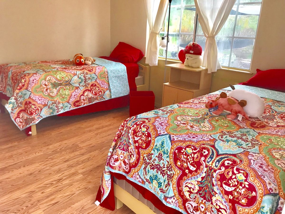A cozy bedroom with twin beds adorned with colorful floral bedding, filled with natural light from the window.
