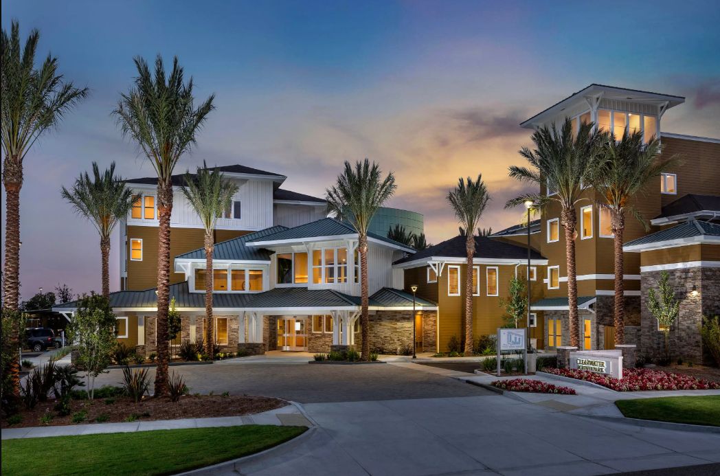 A modern residential building at dusk with palm trees lining the entrance.
