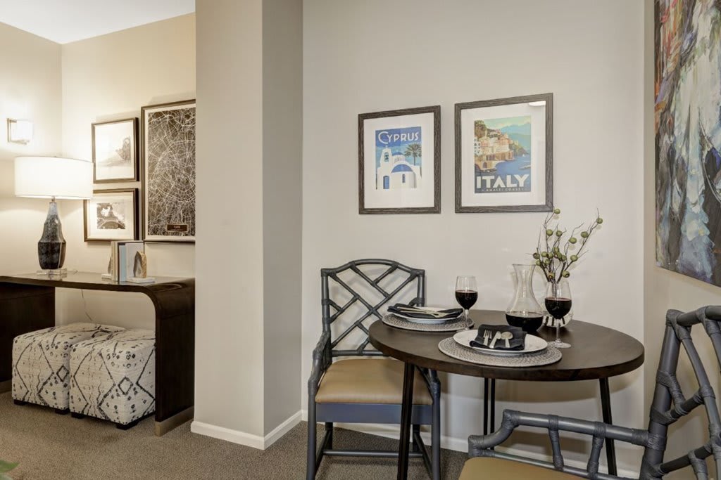 A cozy dining area with a round table and two chairs, adorned with framed artwork on the walls and set for a meal with wine glasses.