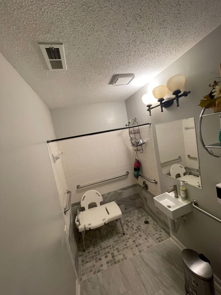 An accessible bathroom with safety features including a shower chair and grab bars.