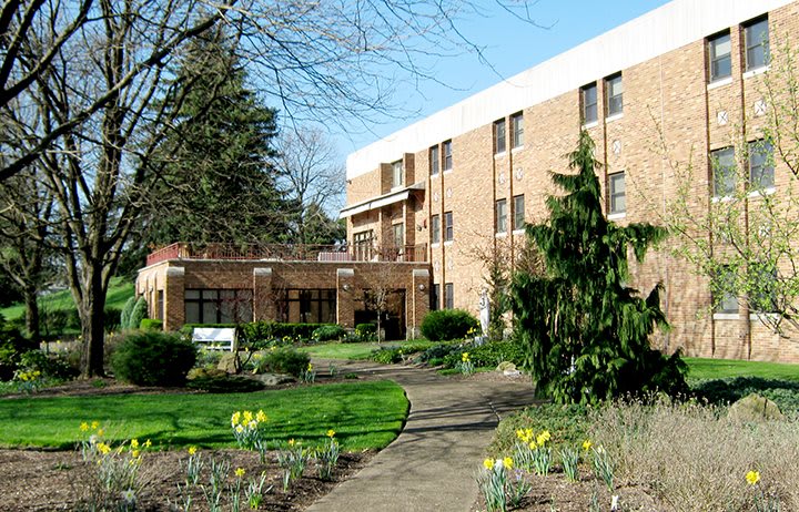 A brick building surrounded by a landscaped garden with trees and a winding pathway.