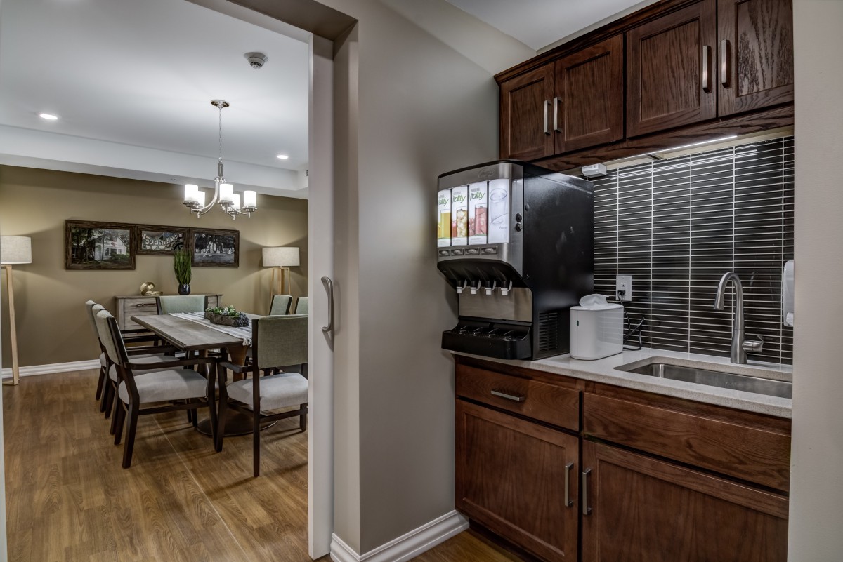 A modern kitchen area with a beverage dispenser and view into the adjacent dining room.