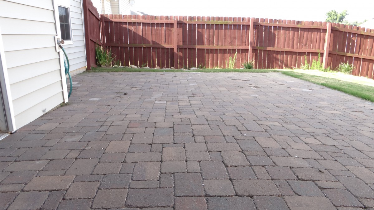 A backyard patio area with stone pavers and a wooden fence.
