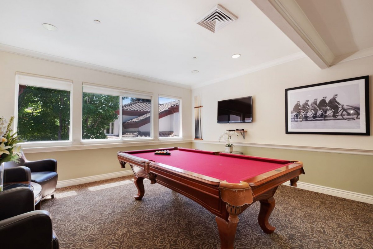 A well-lit game room featuring a pool table with a red felt top and a wall-mounted television.