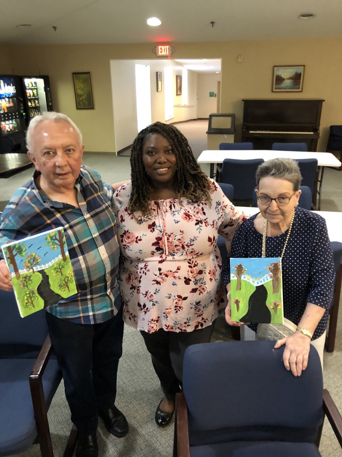 Three people smiling and holding up their paintings indoors.